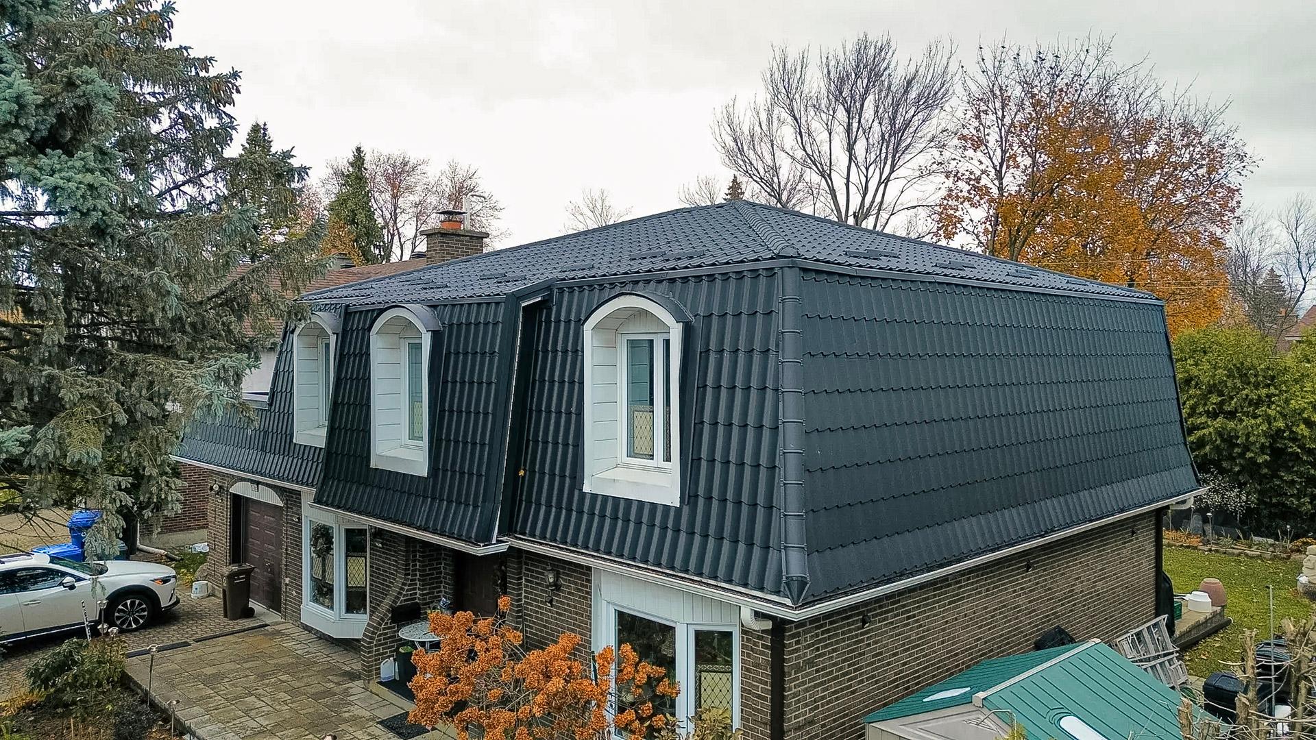 Maison en briques avec toiture en tôle noire style tuiles, lucarnes blanches.