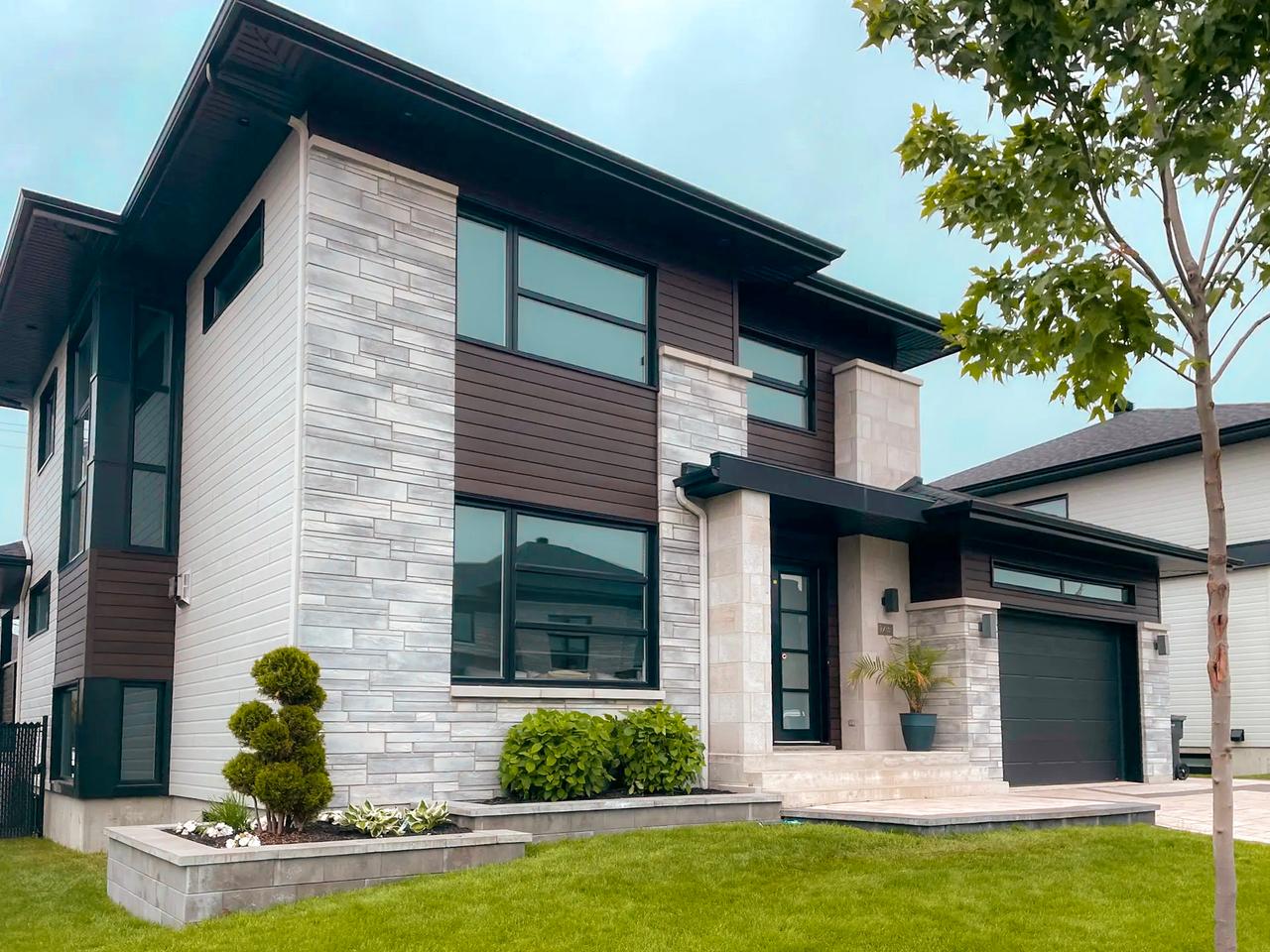 Maison moderne à deux étages avec façade en pierre grise, revêtement en bois brun et garage noir intégré