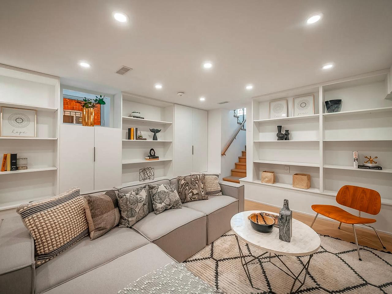 Sous-sol aménagé avec salon moderne comprenant un canapé modulaire, une bibliothèque intégrée, une table basse en marbre, un fauteuil en bois et une décoration minimaliste.