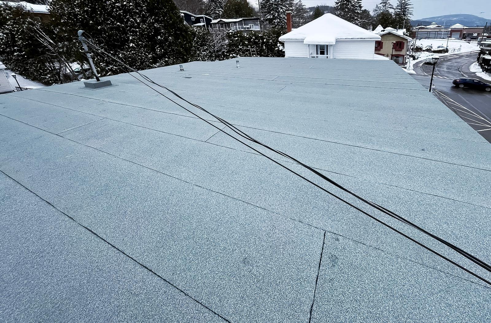 Toiture plate recouverte d’une membrane élastomère grise en hiver avec câbles électriques apparents.