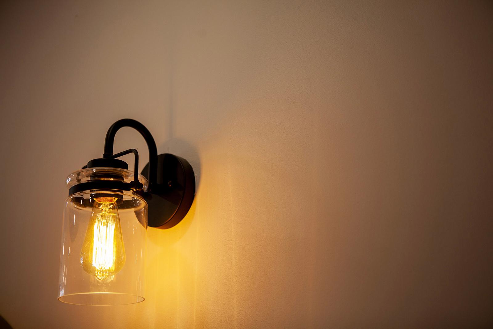 Applique murale noire avec ampoule Edison allumée et abat-jour en verre transparent diffusant une lumière chaude