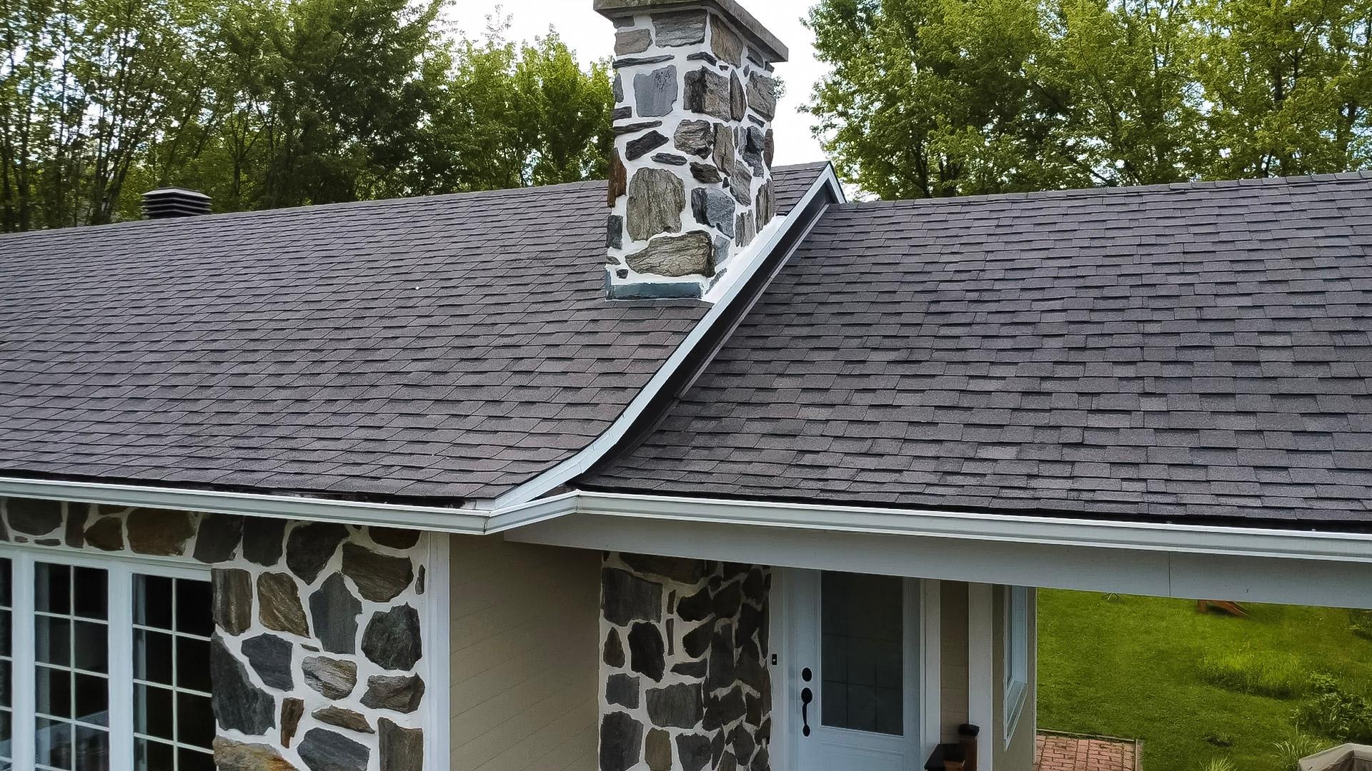 Toiture résidentielle recouverte de bardeaux d’asphalte gris avec évents de ventilation sous un ciel dégagé.
