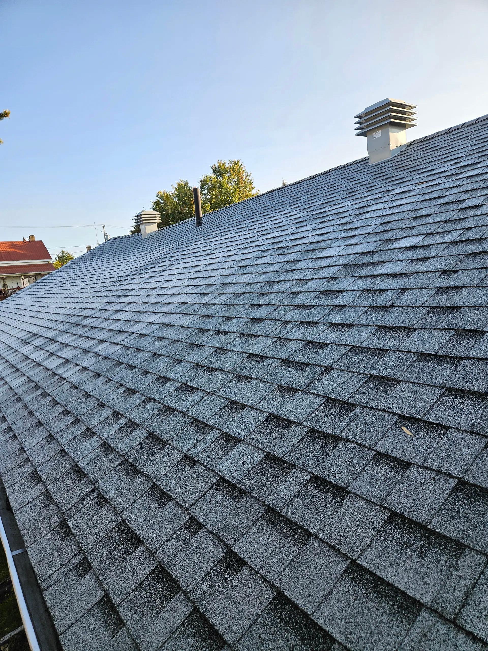 Toiture résidentielle recouverte de bardeaux d’asphalte gris avec évents de ventilation sous un ciel dégagé.