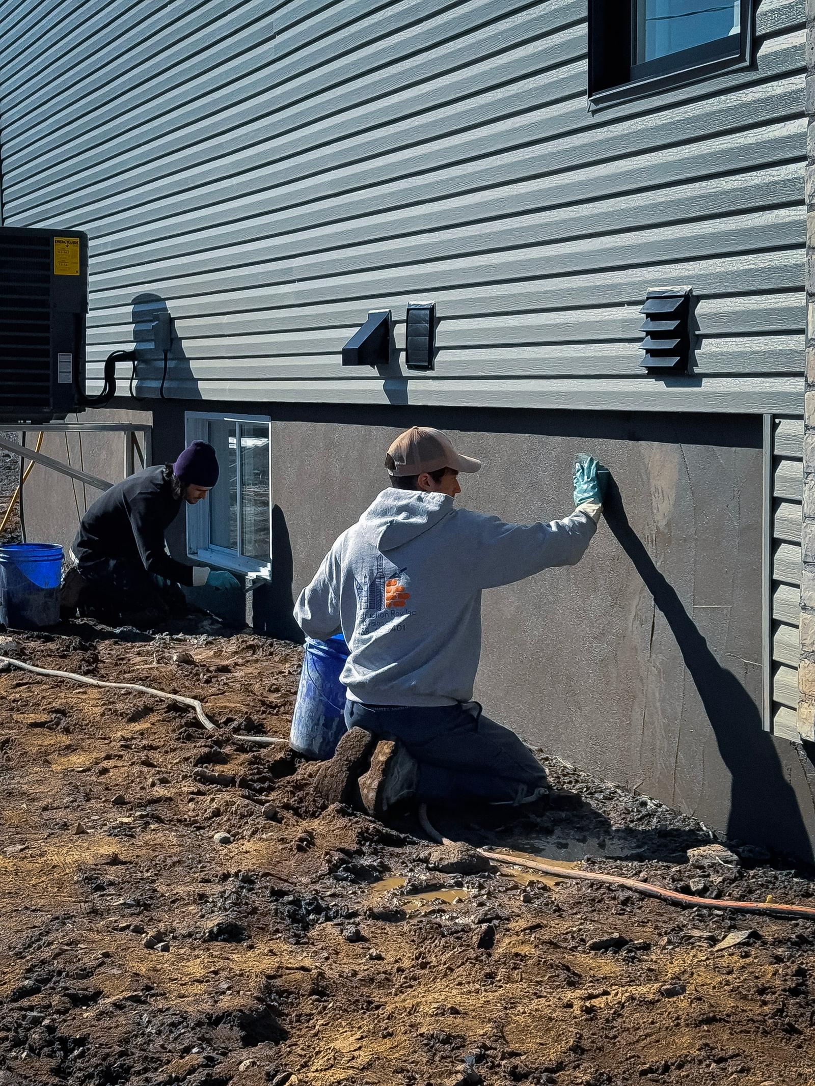 Travailleurs appliquant un revêtement sur une fondation de maison pour réparer des fissures et imperméabiliser