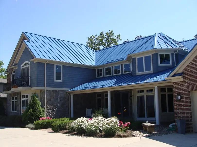 Maison moderne à deux étages avec une toiture en métal bleu à pignon et plusieurs pans, combinée avec un revêtement bleu et une façade en pierre. Le toit en métal offre une finition élégante et durable.
