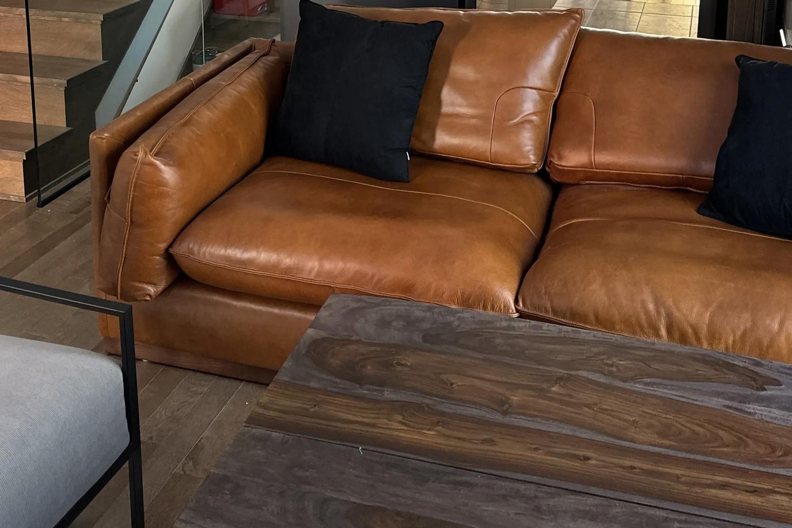 Gros plan sur un canapé en cuir caramel avec coussins noirs, table basse en bois foncé et sol en bois naturel dans un intérieur moderne.