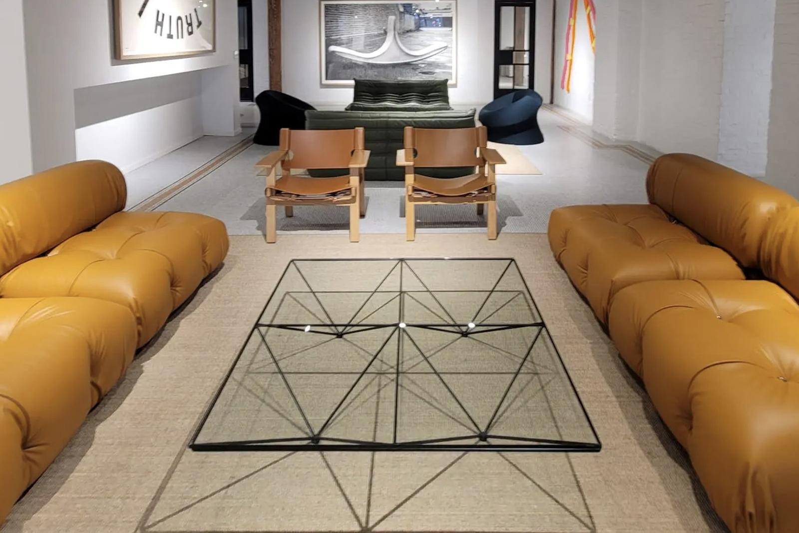 Salon au style industriel avec canapés en cuir capitonné jaune, table basse en verre géométrique, œuvres d'art murales.