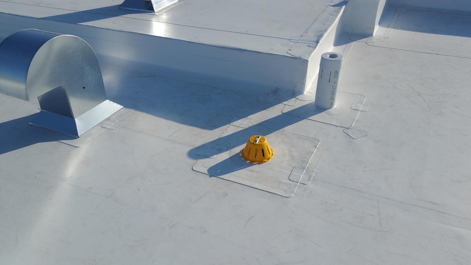 Toiture plate en membrane blancheen TPO avec sorties de ventilation, drain protégé par un couvercle jaune et détails d’étanchéité visibles.