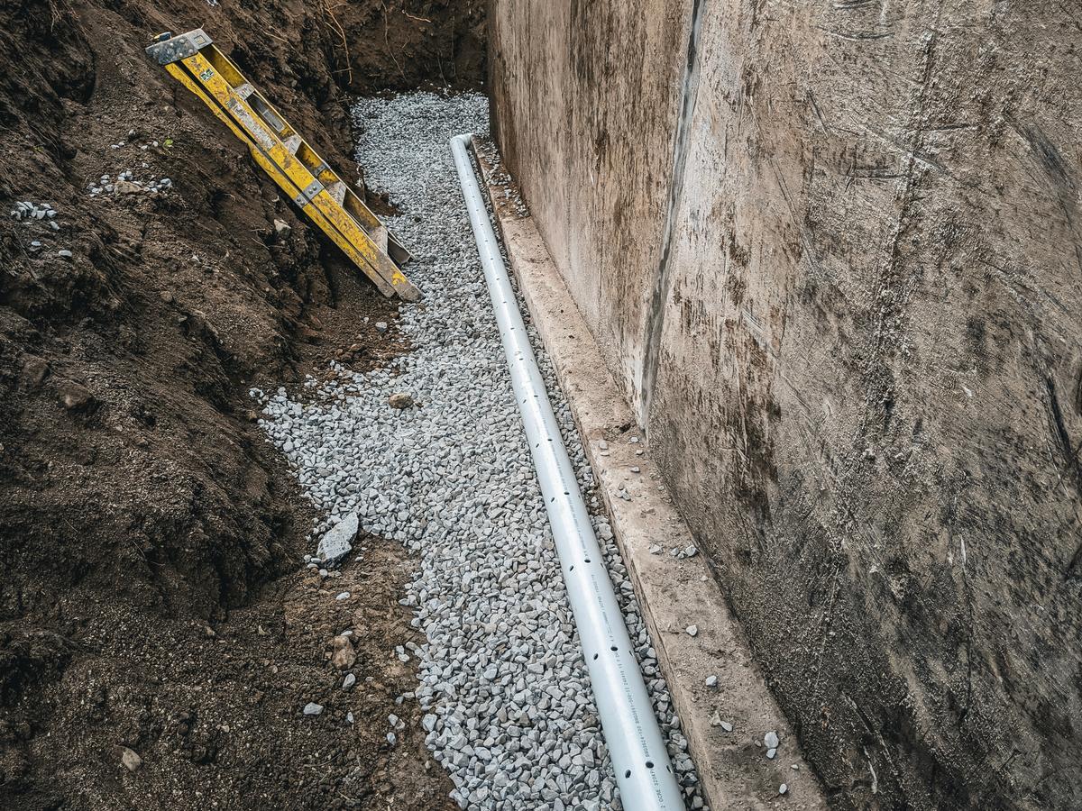 Installation d’un drain français en PVC perforé avec gravier le long des fondations d’une maison.