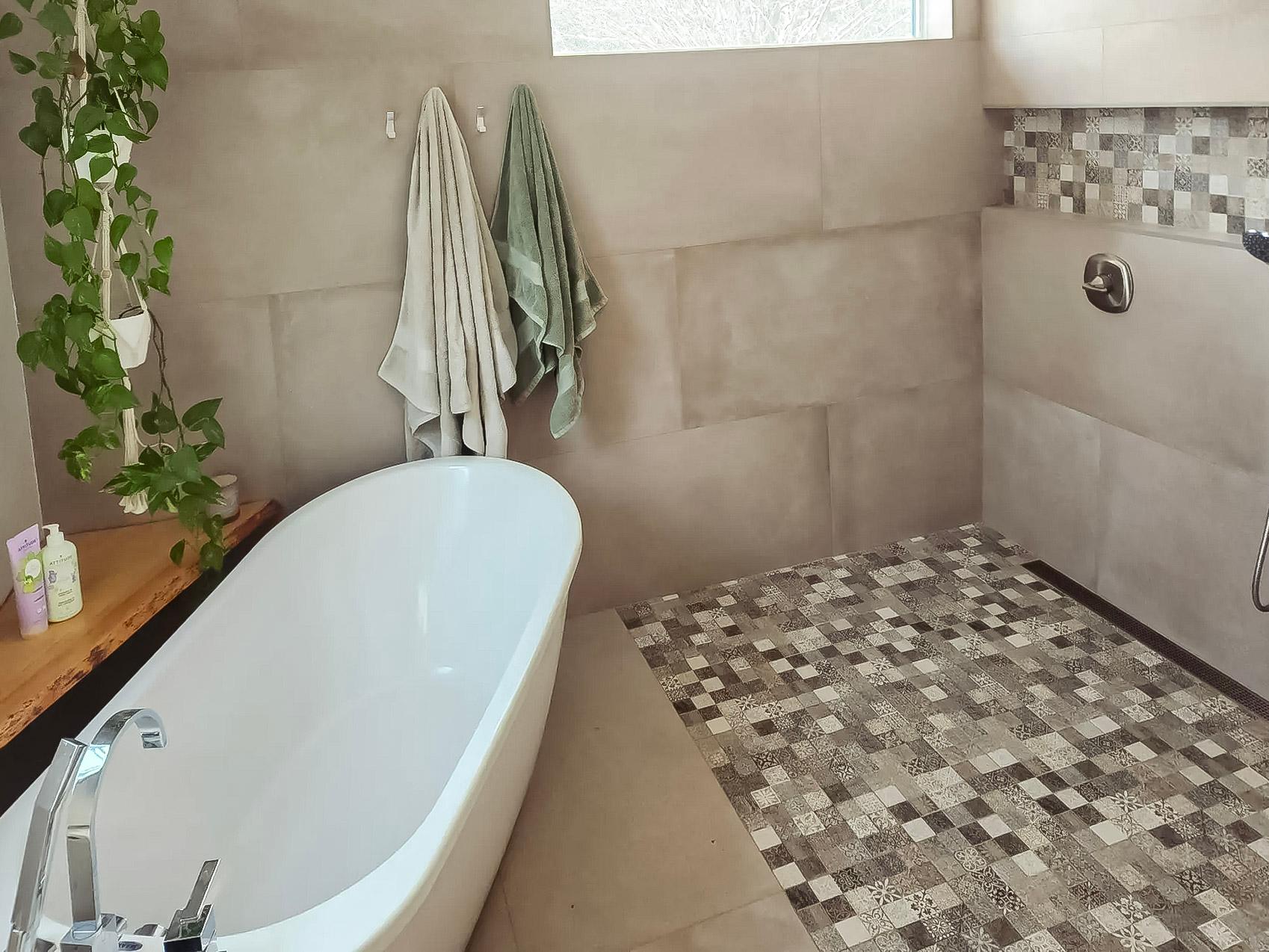 Salle de bain moderne avec baignoire autoportante, douche à l’italienne, carrelage en mosaïque et décoration végétale naturelle.