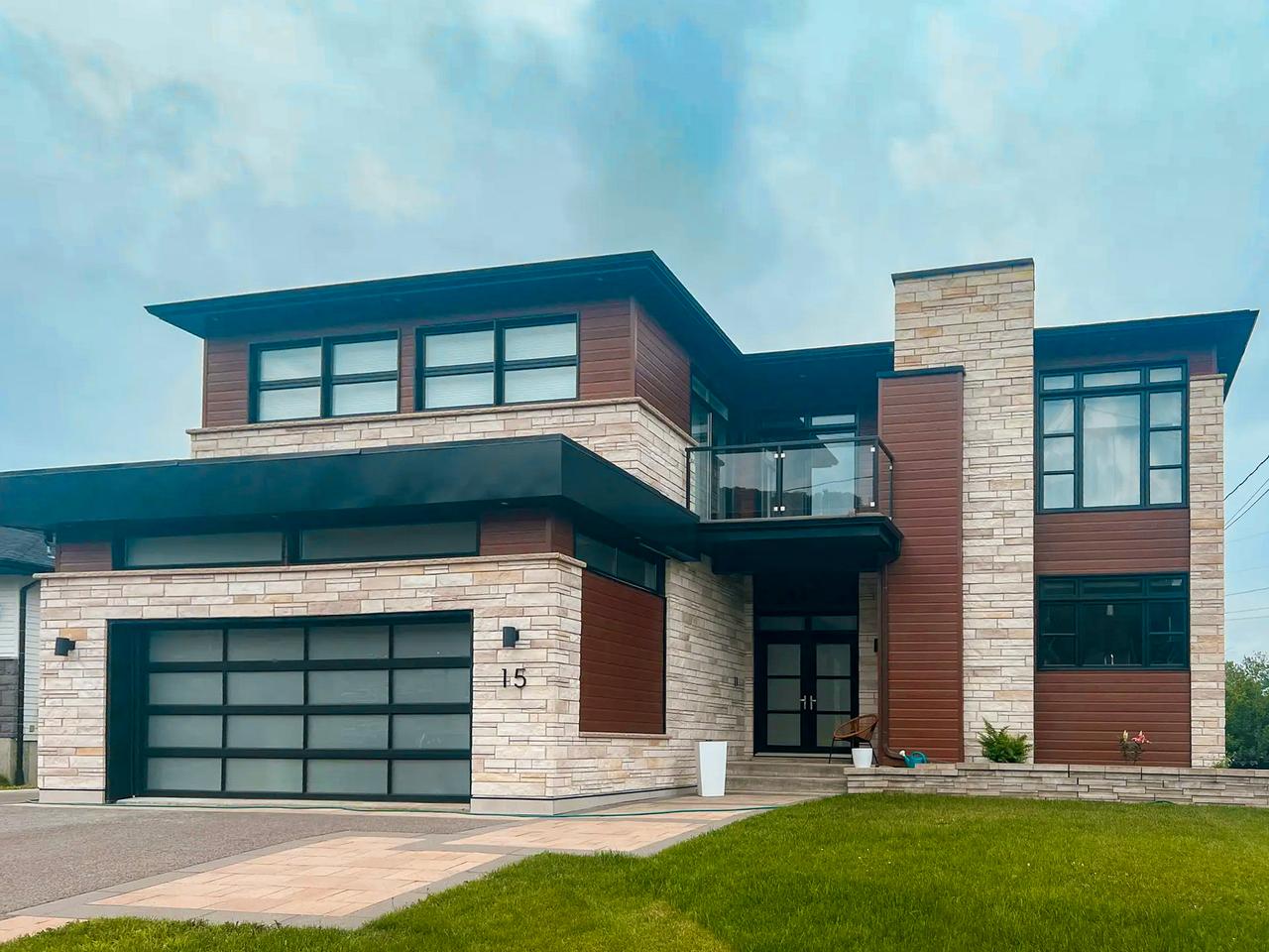 Maison contemporaine à deux étages avec façade en pierre et bois, garage vitré et balcon en verre