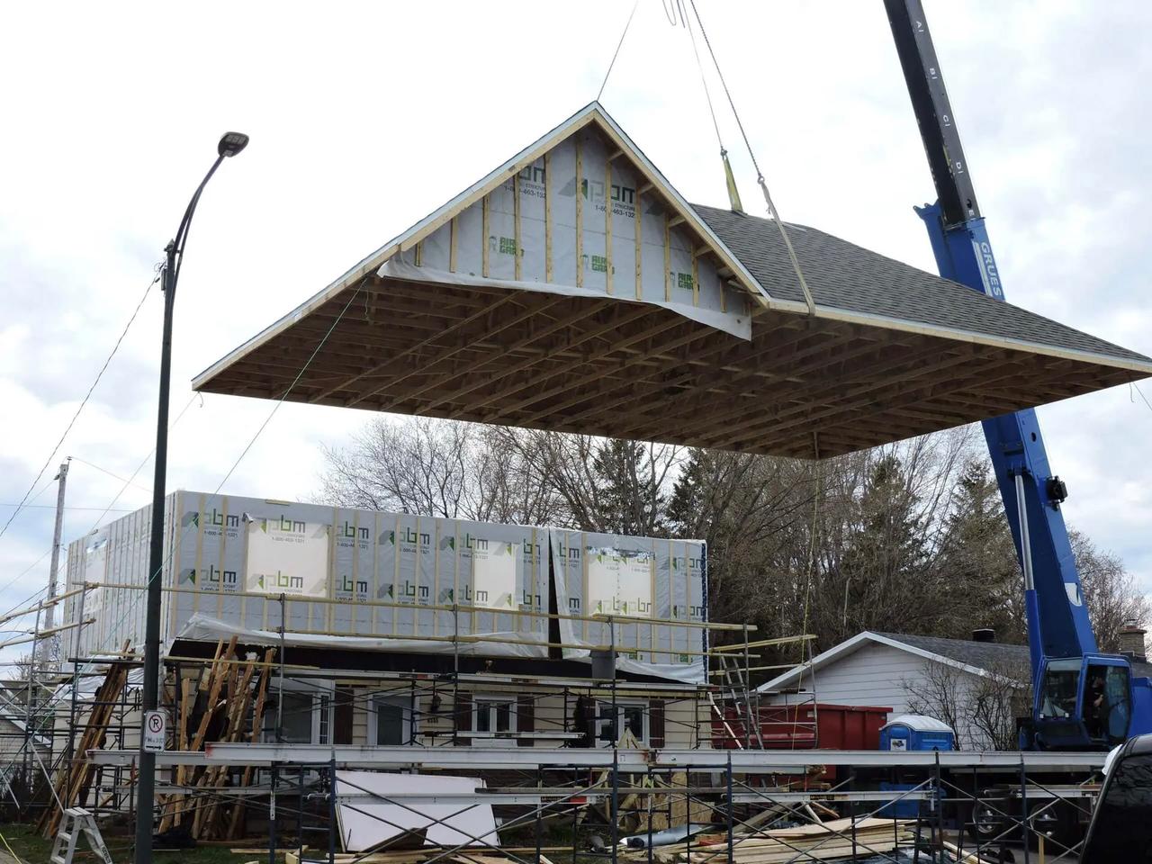 Levage d’un toit préfabriqué par une grue pour l’installation sur un agrandissement résidentiel en construction.