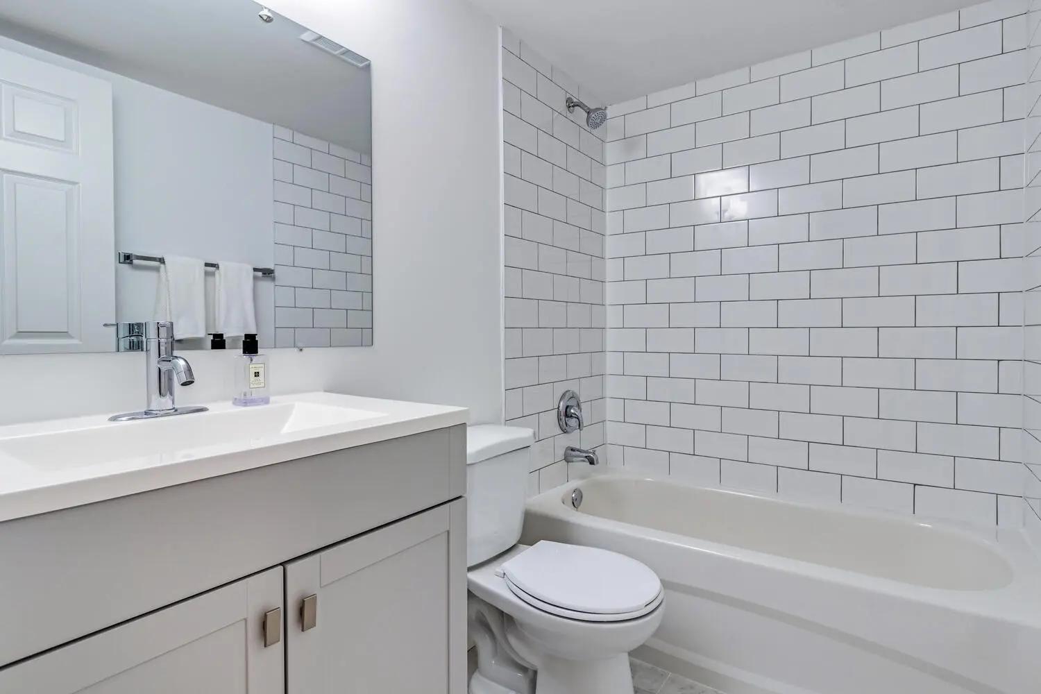 Salle de bains propre et fonctionnelle avec une baignoire et une douche, des murs carrelés blancs et des armoires de rangement