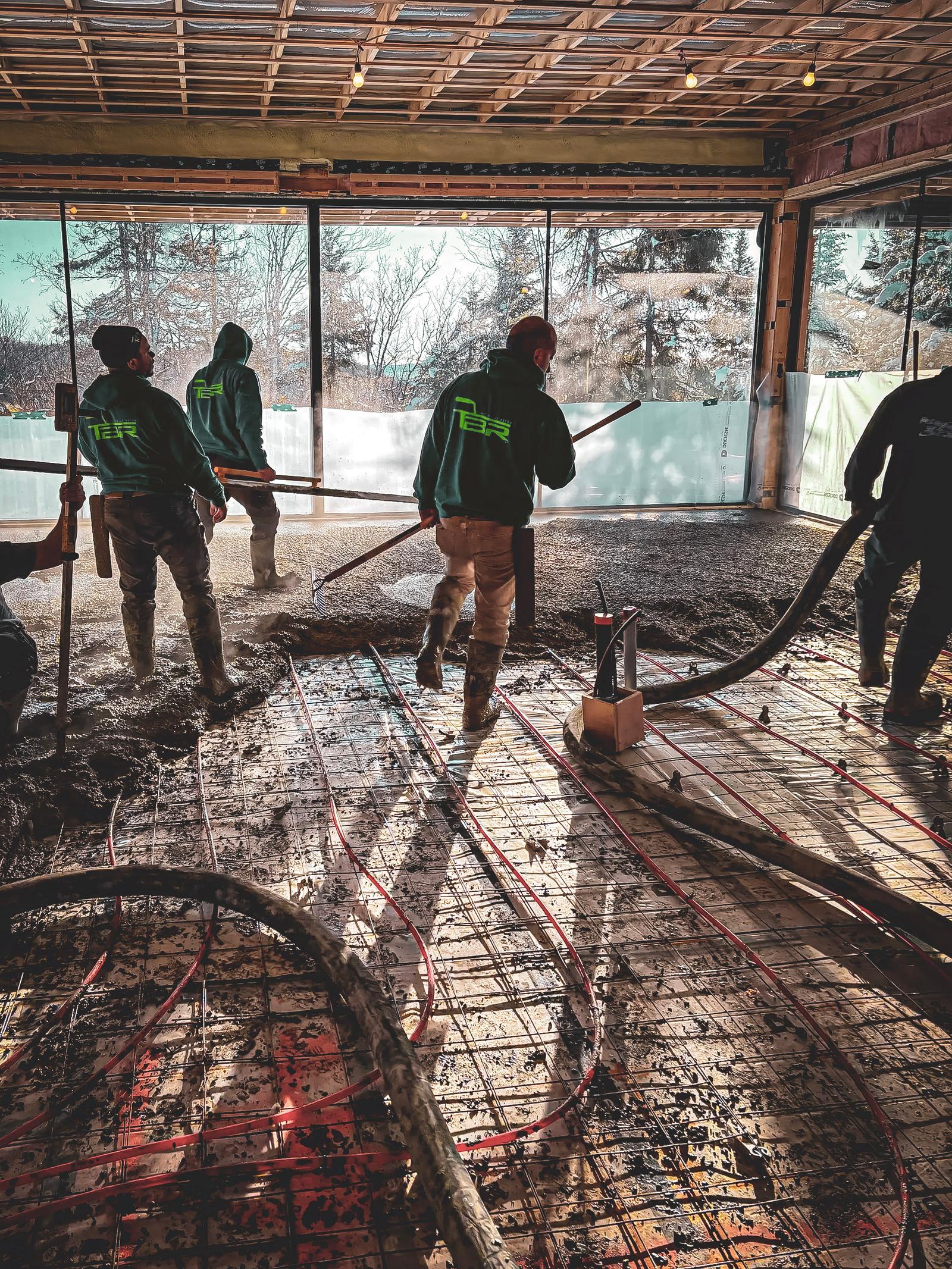 Travailleurs posant une dalle de béton dans un bâtiment en construction avec un système de chauffage au sol visible.