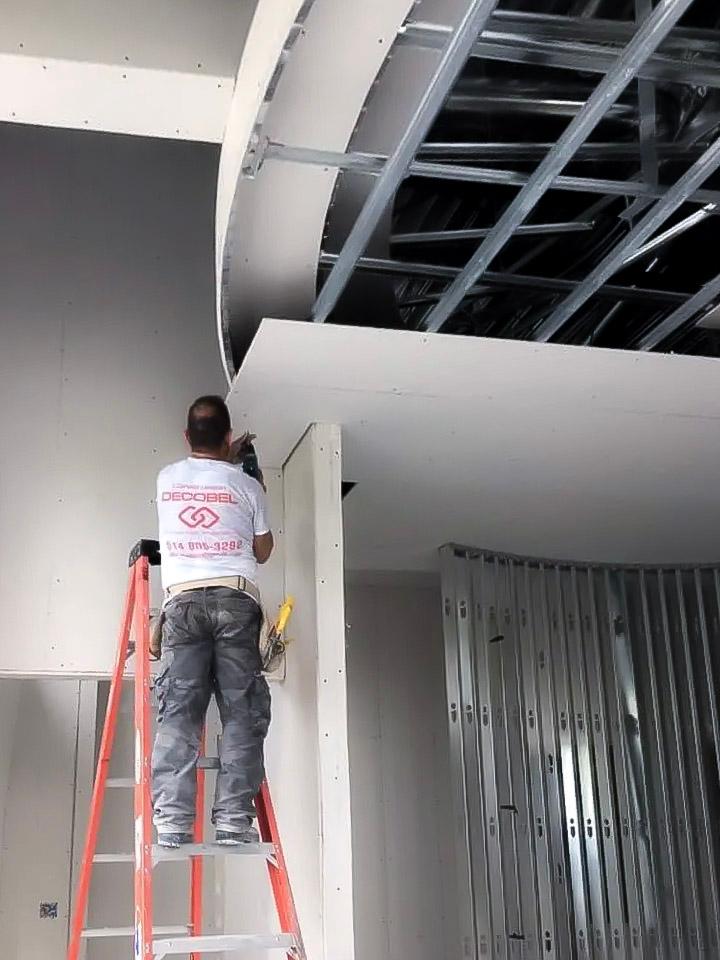 Ouvrier fixant des plaques de plâtre sur une structure métallique dans un projet d'aménagement intérieur.