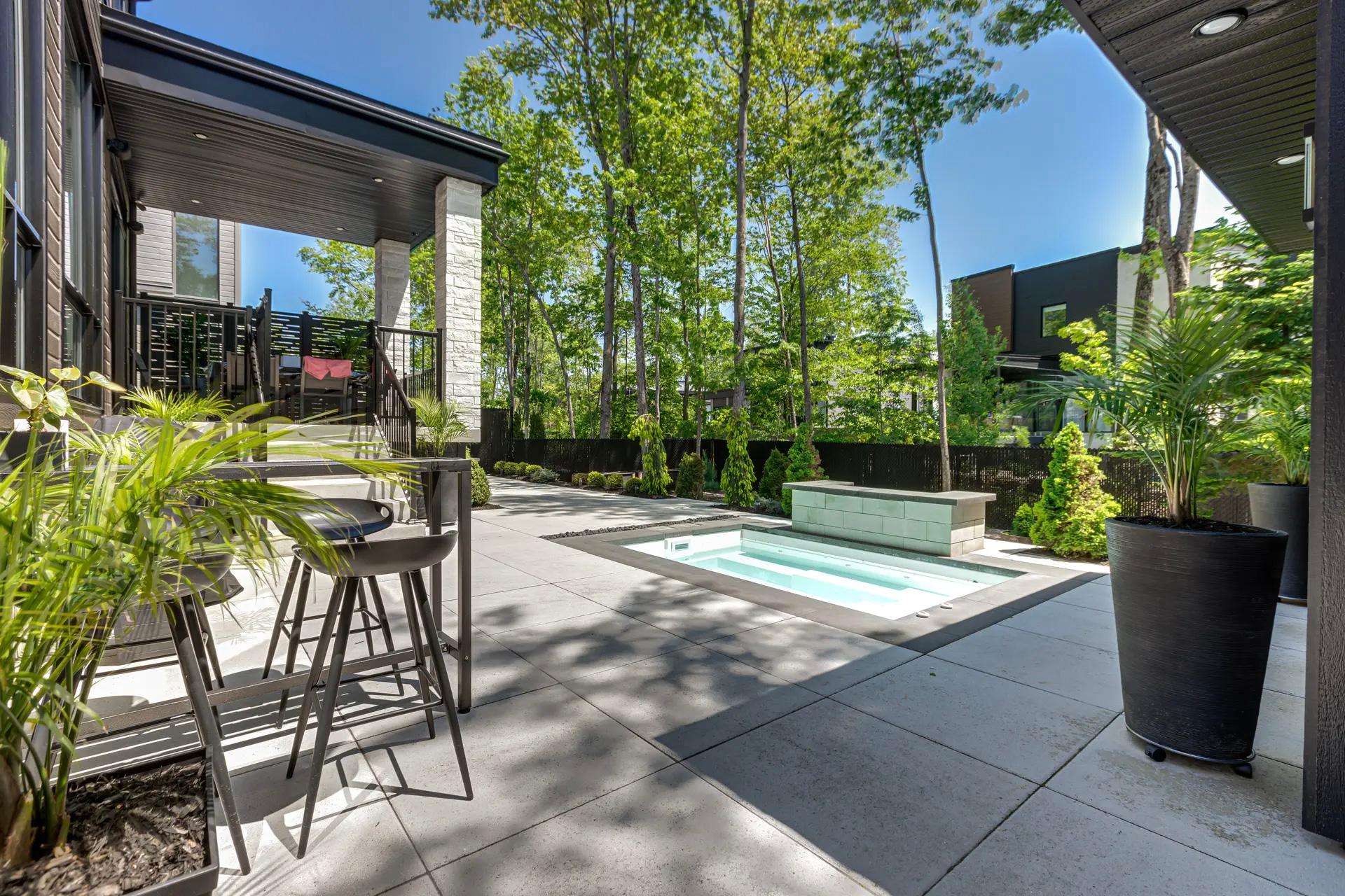 Cour arrière moderne avec spa intégré, grande terrasse en béton, mobilier extérieur et végétation luxuriante