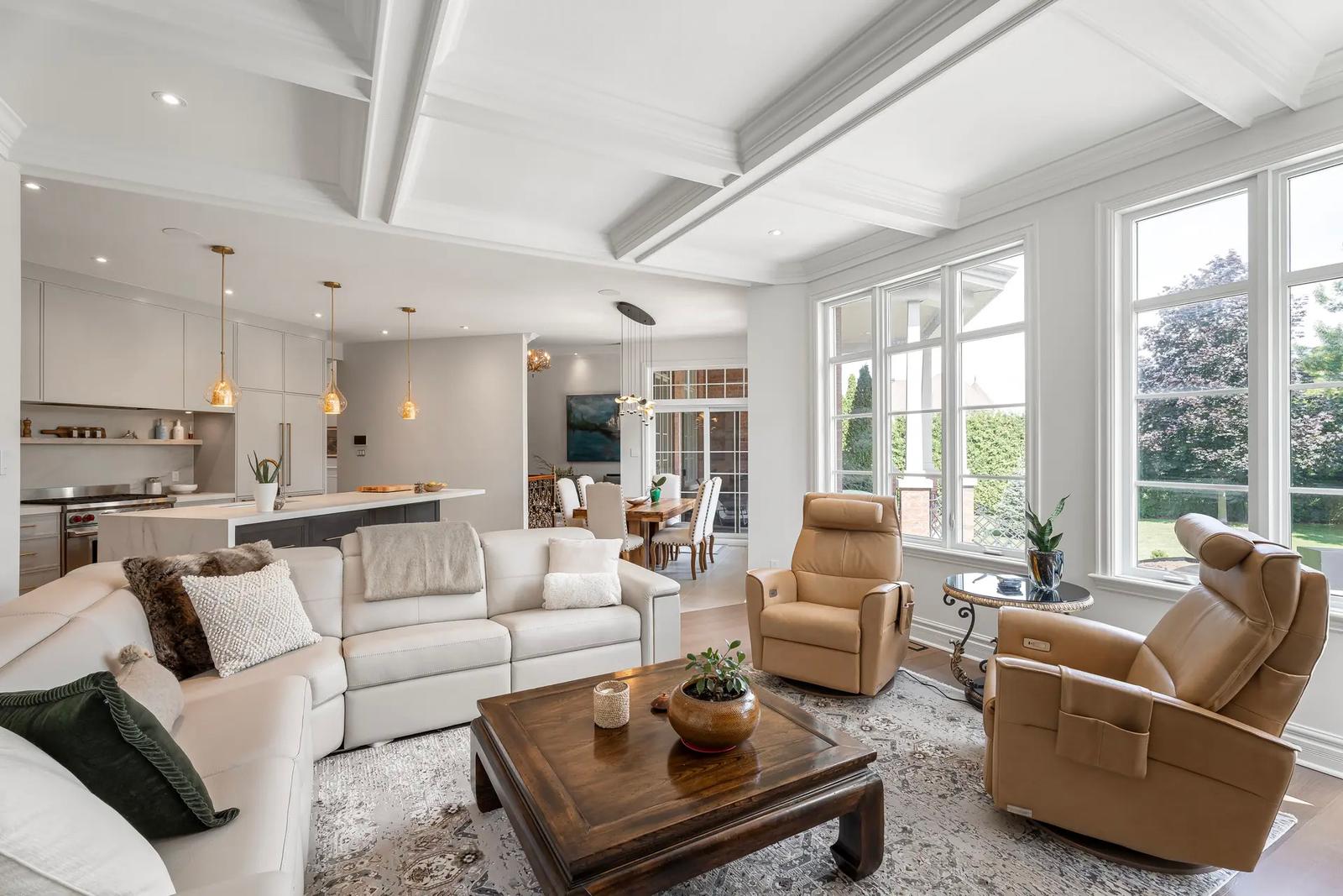 Salon lumineux avec canapé d'angle, fauteuils en cuir, et grandes fenêtres dans un espace ouvert.
